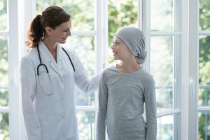 Happy doctor supporting positive child with cancer wearing headscarf